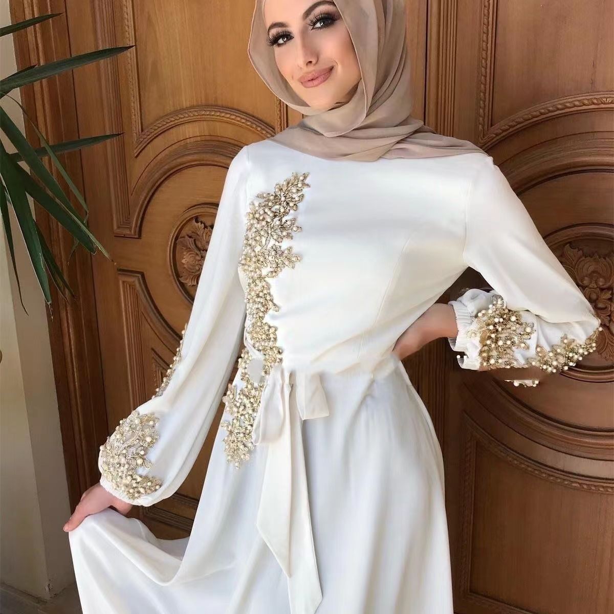 Woman wearing a white dress with gold embellishments in a room with wooden paneling.